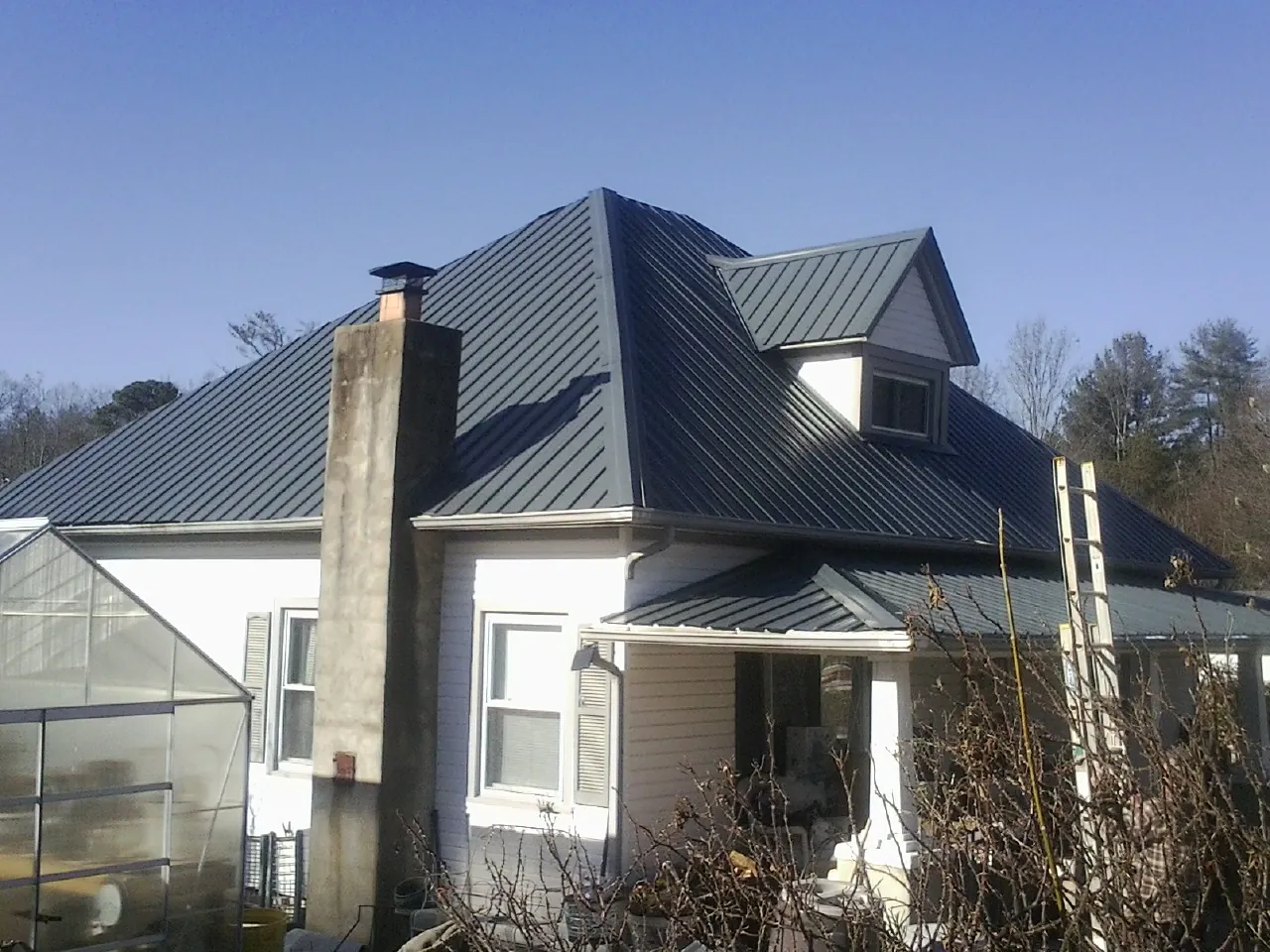 Dark blue standing seam metal roof on a white farmhouse with dormer — Slate & Tile Roof Repair by Roofing Brothers in Burnet
