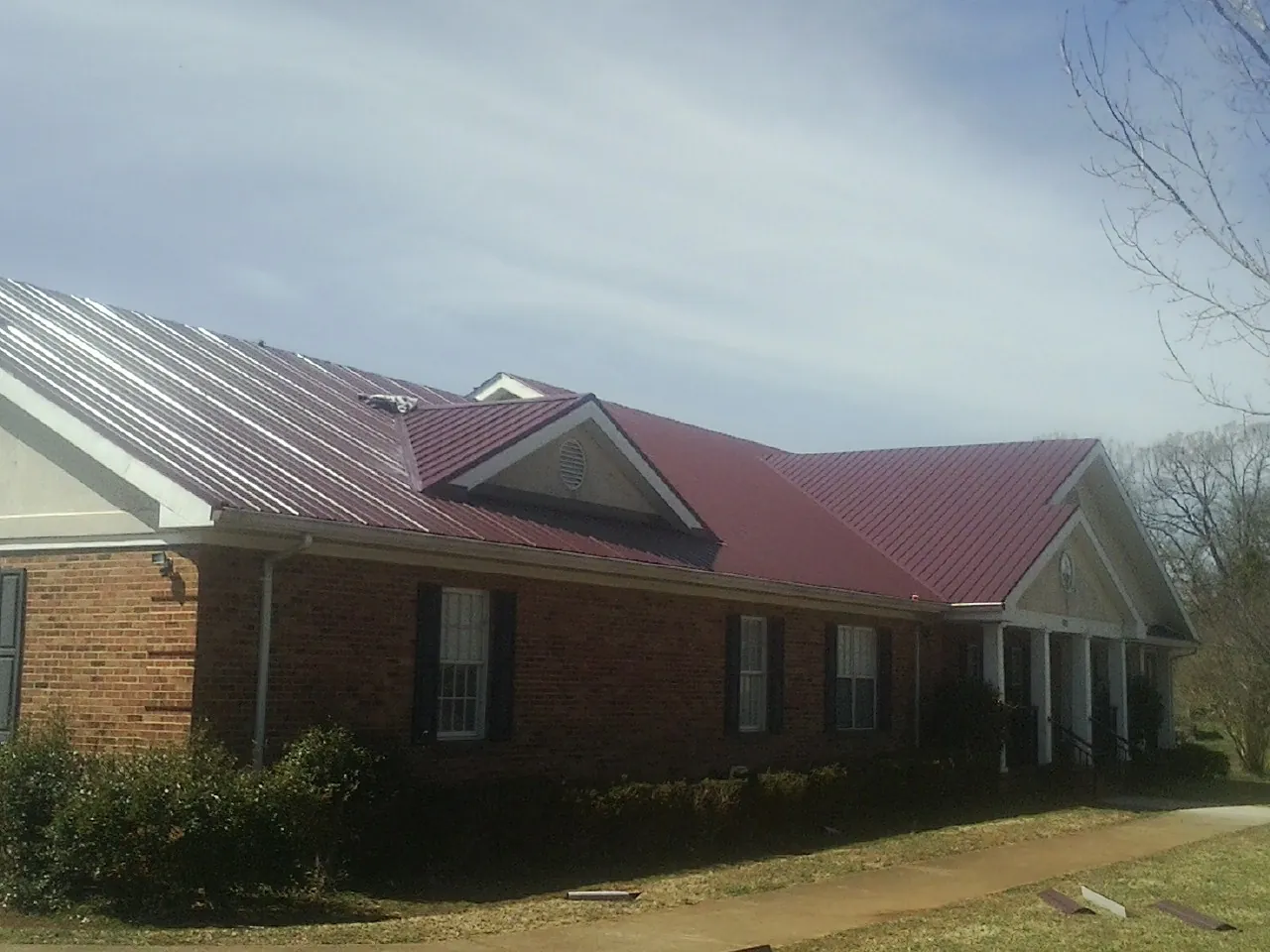 Red metal roof with gabled entries on a long brick building, from a Hail Damage Roof Repair job in Burnet