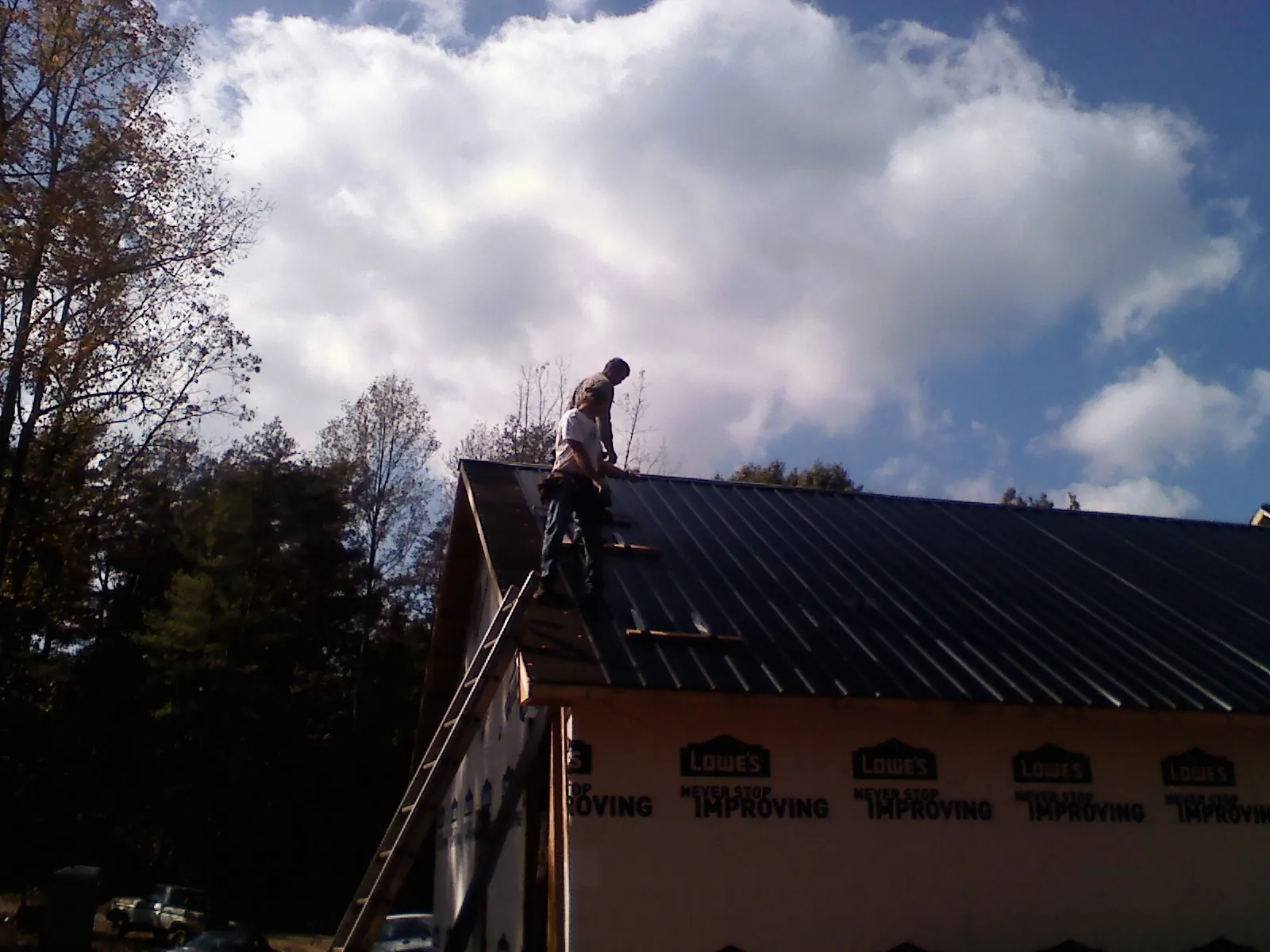 Roofer fastening dark metal panels high against a cloudy sky, from a Roof Inspection job in Burnet