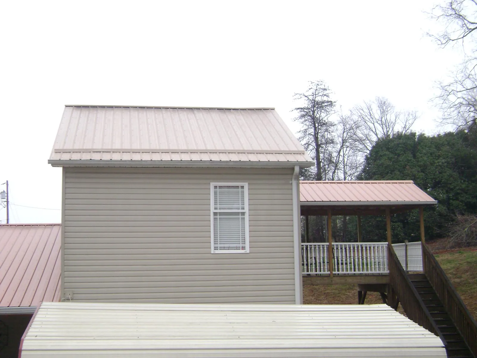 Tan metal roofs on a two story addition and attached porch, from a Roof Replacement job in Burnet